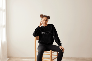 woman wearing black sweatshirt sitting on chair - sweatshirt says "banned books are my favorite"